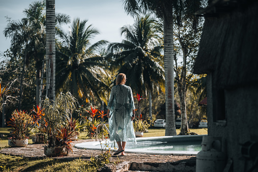 Rear view of a woman in a turquoise sundress walking between the pool and palm trees