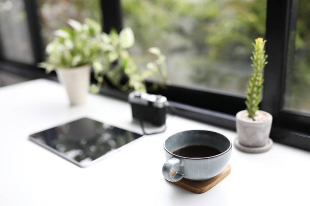 istock Blue coffee cup and tablet and plants in front of window 1385481961