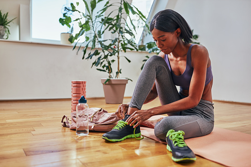 Afro woman just finished training at home and putting on sneakers