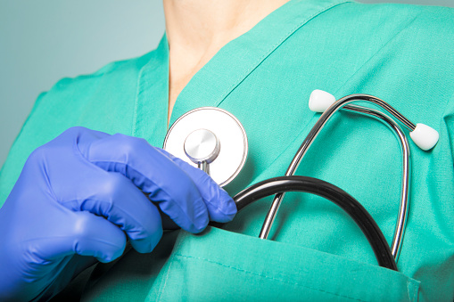 A close up of a medical worker wearing scrubs taking a stethoscope from pocket.