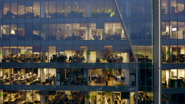 Windows of offices in a glass skyscraper at night.