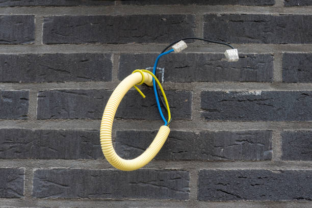 Electrical conduit from greay brick wall From a gray brick wall protrudes a yellow flexible electrical conduit containing different colored wires with transparent welding caps on the ends. biddinghuizen stock pictures, royalty-free photos & images