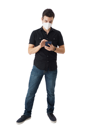 Full shot of a young latin man with a face mask standing and using a mobile phone.