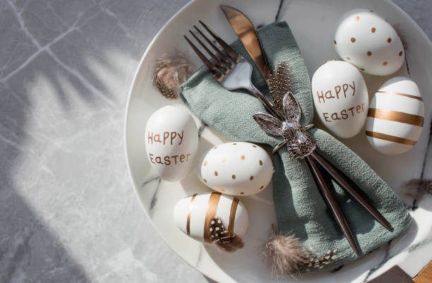 istock Banner. Table setting. A fashionable marble plate with a rabbit on a napkin, Easter eggs and feathers on a gray background. Top view. Happy Easter holiday concept for cafes and restaurants. 1385504441