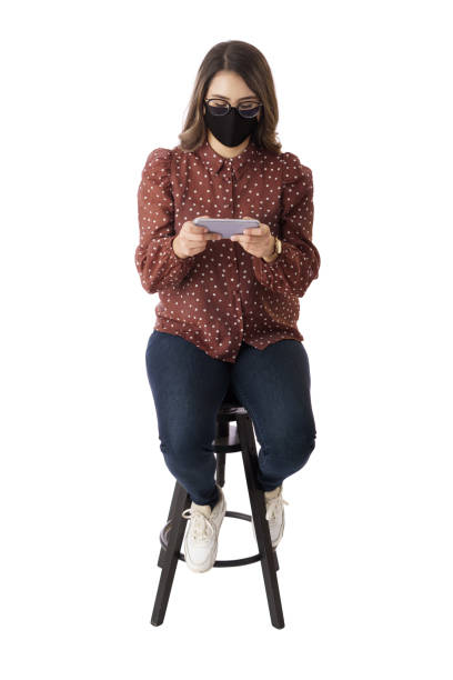 mujer joven con máscara sentada y usando el teléfono - isolated on white full length red protection fotografías e imágenes de stock