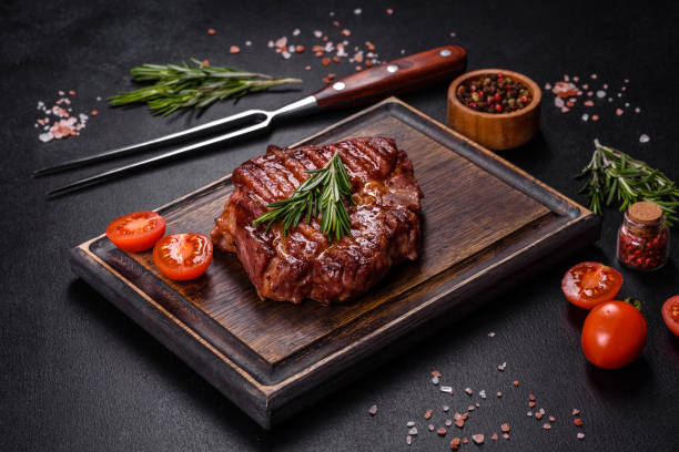 istock Grilled ribeye beef steak, herbs and spices on a dark table 1385507605