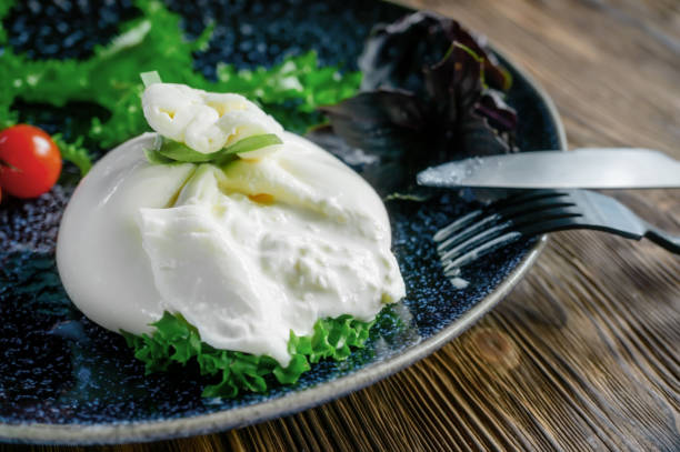 Traditional Italian dish of burrata Stratocell. Burrata on a dark plate is served for a romantic dinner with tomatoes and arugula. stock photo