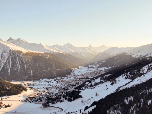 A sunset casts a warm glow on a snow-covered mountain peak with a valley below.