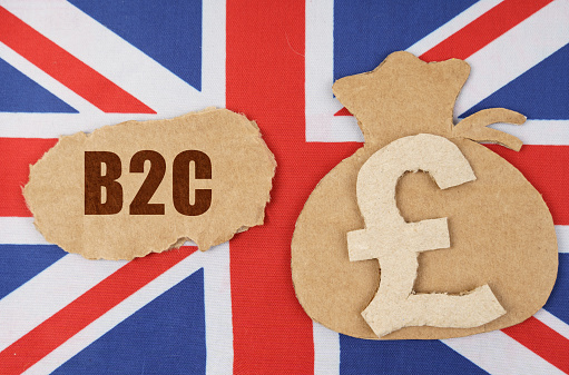 The concept of national economy and business. On the flag of Great Britain lies a cardboard figure of a bag with a money symbol and a cardboard with the inscription - B2C