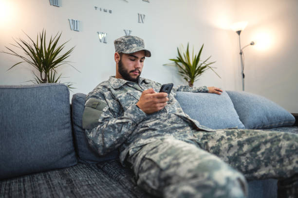 istock Soldier sitting on sofa in living room and using a smartphone 1385515004