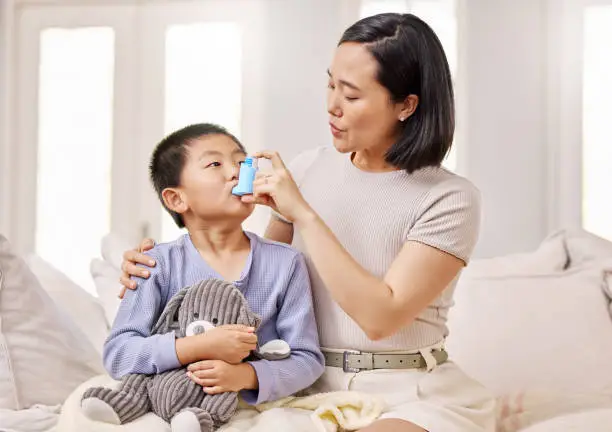 Photo of Shot of a woman helping her son with his asthma inhaler