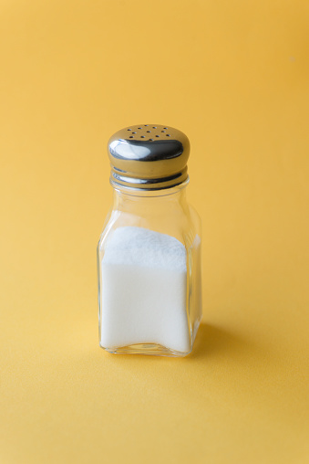 Salt shaker with salt on yellow background.
