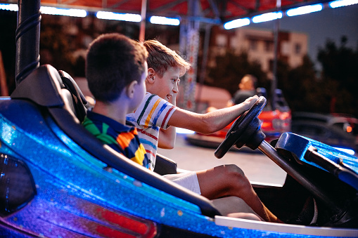 Boys having fun driving bumper car at amusement park