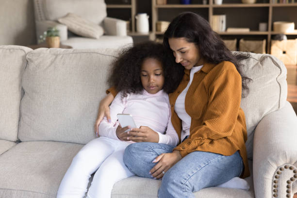 istock Smiling affectionate young African American mother and daughter using cellphone. 1385517851