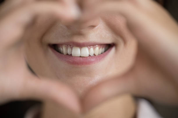 Close up happy young woman showing healthy smile. Close up happy young woman making heart sign, showing straight white teeth, feeling with professional dental services. Thankful millennial female client demonstrating healthy teeth, oral care concept. tooth enamel stock pictures, royalty-free photos & images