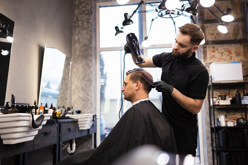 Master cuts hair and beard of men in the barbershop, hairdresser makes hairstyle for a young man