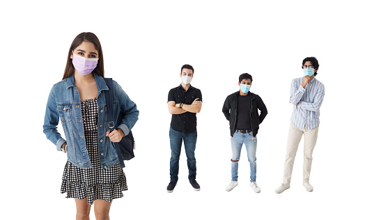 A latin female student with a face mask standing next to her male classmates and looking at the camera.