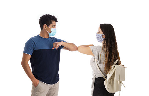 Two latin students wearing face masks and greeting each other with their elbows.