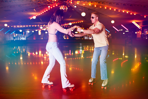 Young couple disco dancing at the retro roller skating rink.