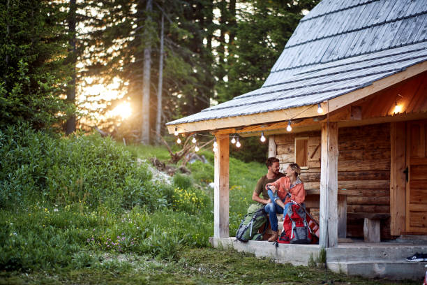 A young couple in love spending time together at the cottage porch in the forest. Vacation, nature, cottage, relationship A young couple in love spending time together at the cottage porch in the forest on a beautiful day. Vacation, nature, cottage, relationship cottage life stock pictures, royalty-free photos & images