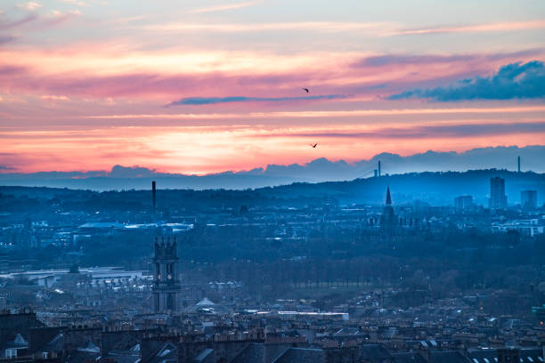 A classic view of Edinburgh from Calton Hill, featuring the iconic Dugald Stewart National Monument in the foreground. The city’s skyline glows under the vibrant hues of a colorful sunset, with illuminated streetlights enhancing the historic charm of Scotland’s capital. A timeless travel scene capturing Edinburgh's beauty.