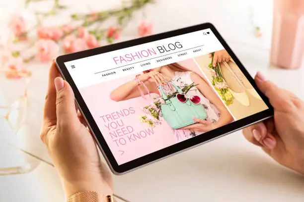 Photo of Fashion blog website on tablet in womanâs hands. Spring outfit accessories trends - made up content.