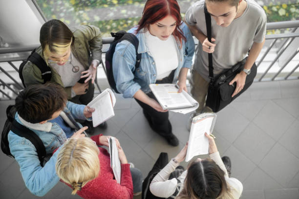 Group of high school students sitting on stairs in school building and preparing for exam or class. They are wearing casual clothes and looks happy. Photo taken from above.