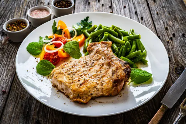 Fried pork chop with boiled green bean and fresh vegetable salad on wooden table