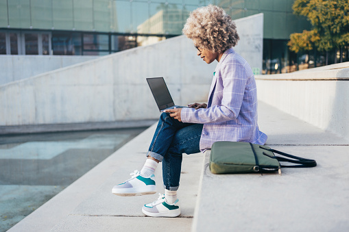 Black female business woman working on a laptop writing emails outdoors in the city