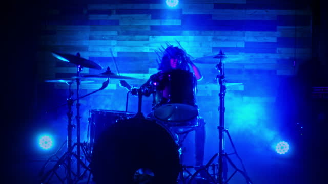 Drummer girl energetically playing the drums in blue, red and green lights.