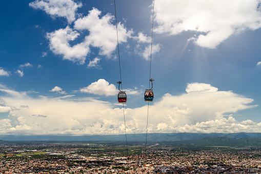Salta, Argentina - January 4, 2021: Two cable car cars cross each other on the San Bernardo hill with the capital of the northern province in the background