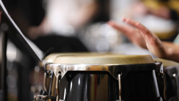 Close up of moving hands playing congas or percussion instrument in a band A close up of hands moving or in motion playing the congas or bongo style drums in a percussion section of a band or orchestra. Drum skin in focus. drummer hands stock pictures, royalty-free photos & images