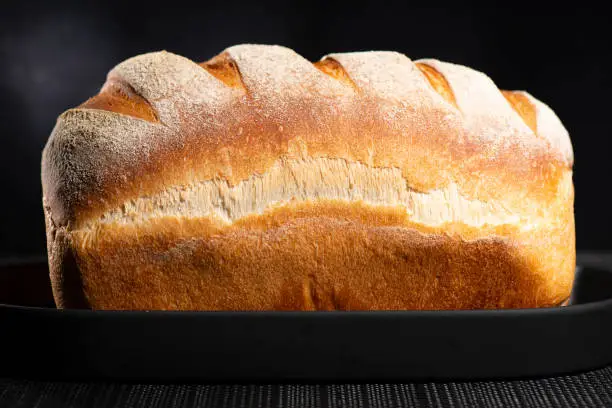 Freshly baked continental bread loaf dusted in white flour with five scores a crusty exterior and nice oven spring.