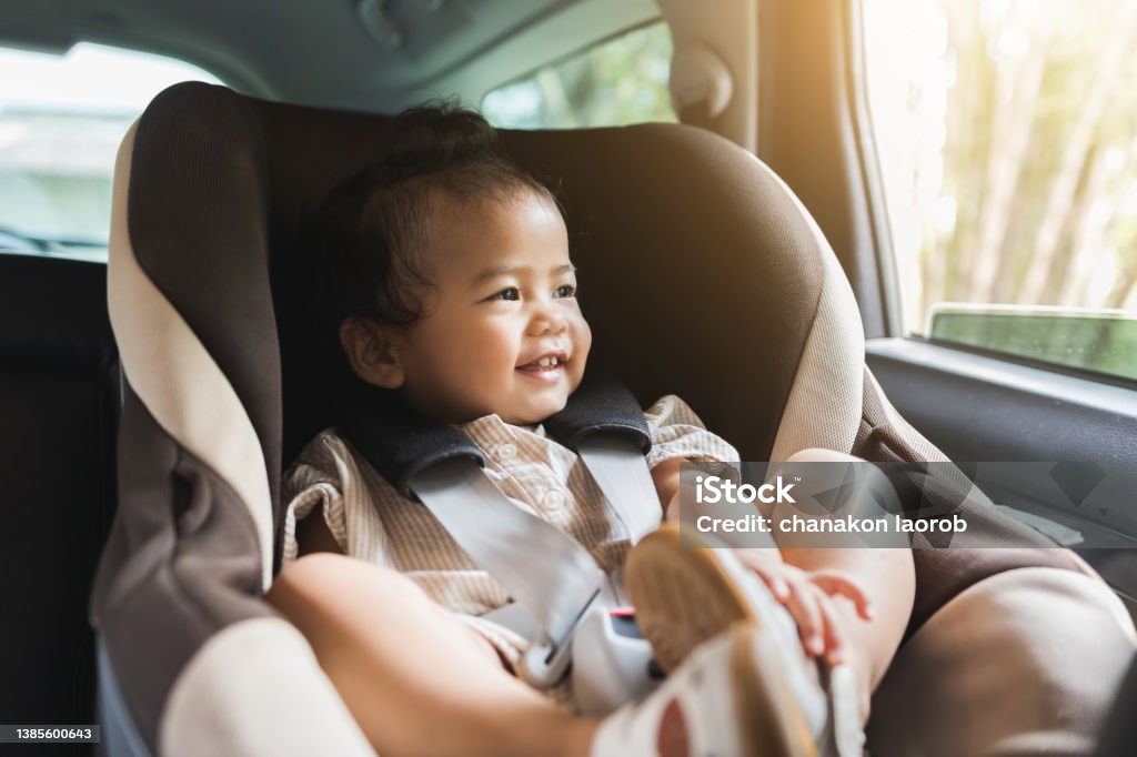 Asian Baby Toddler girl sitting in car seat and looking through window. Infant baby with safety belt in vehicle. Safety car. Family travel concept Car Safety Seat Stock Photo