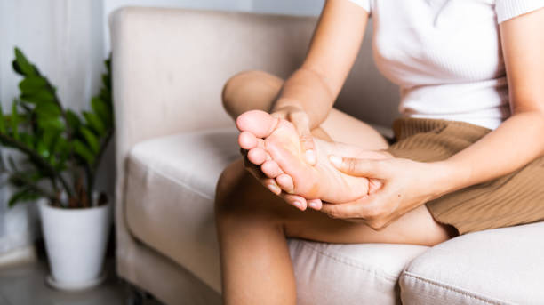 Asian woman sitting on sofa feeling pain in her foot at home stock photo