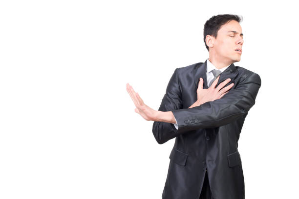 Injured male with outstretched arm in studio Harmed man in formal suit touching chest with hand while standing with closed eyes isolated on white background in studio man-hand-on-chest stock pictures, royalty-free photos & images