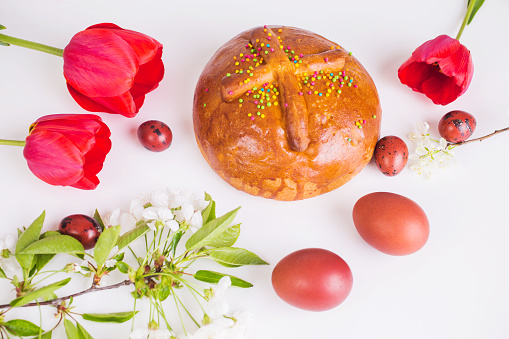 Traditional church holiday. Easter bread. Food on white background. Colored chicken and quail egg. Fresh bakery. Healthy food. Red egg. Tulips and cherry flowers