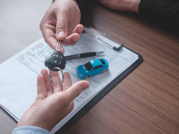 Concept car rental. Close up view Hand of agent giving car key to customer after signed rental contract form.