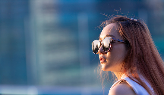 Asian woman with ginger hair wearing sunglasses while looking directly toward the sun