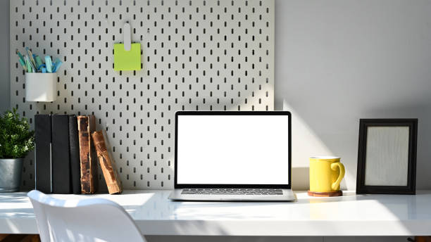 istock Front view computer laptop, stationery, books and picture frame on white table. 1385625279