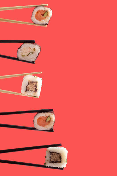 istock Vegetarian sushi minimal concept with vertical creative copy space. Many chopsticks on left side with plenty piece of rolled in nori dried edible seaweed with rice salmon and rice cubes. Lovely red background 1385625302