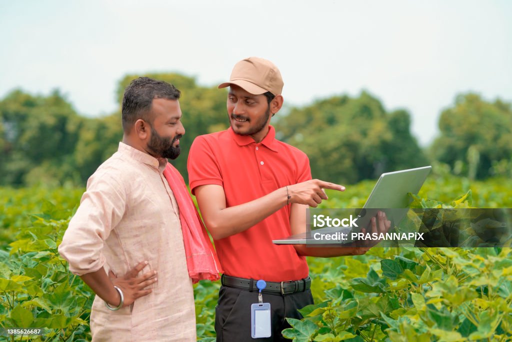 Young indian agronomist showing information to farmer in laptop at green agriculture field. Agronomist Stock Photo