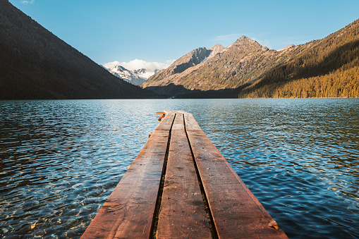 Wooden plank boat pier on a picturesque mountain lake. A place for relaxation and fishing