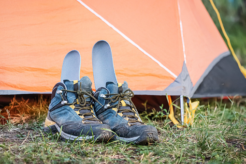 A pair of wet and dirty hiking boots are drying near the tent with the insole sticking out