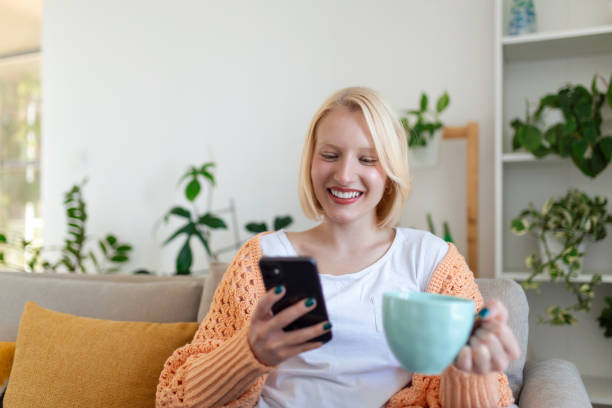 istock Attractive smiling woman using smart phone while sitting on the sofa at home. Communication and coziness concept. 1385631530