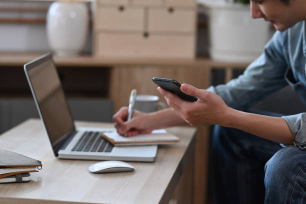istock Young man holding smart phone and writing ideas in a notebook. 1385632250
