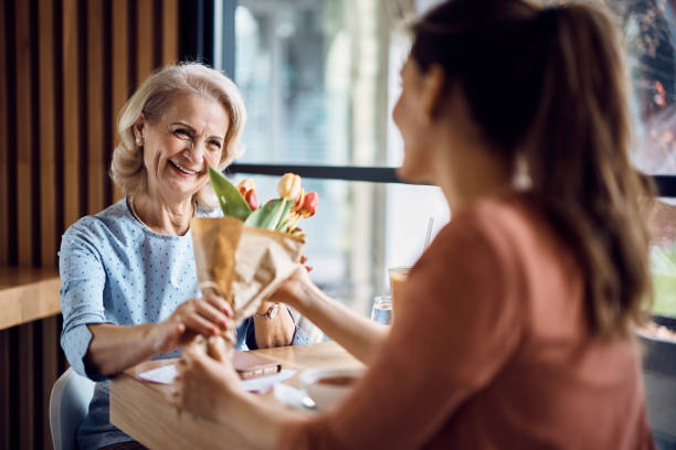 happy senior woman receiving bouquet of flowers from her daughter on mother's day. - bouquet mothers day tulip flower imagens e fotografias de stock