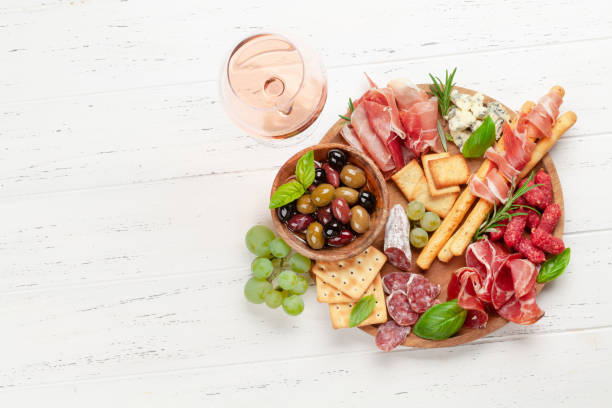 Antipasto board with prosciutto, salami, crackers, cheese, olives Antipasto board with prosciutto, salami, crackers, cheese, nuts, olives and rose wine. Top view flat lay with copy space antipasto stock pictures, royalty-free photos & images