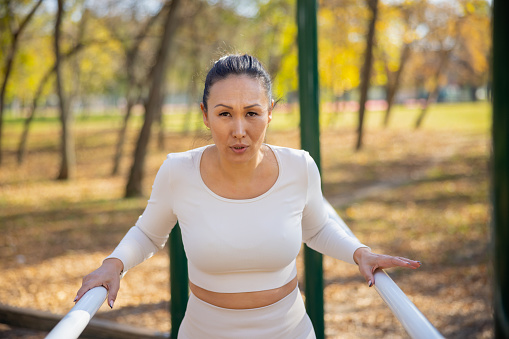 Asian woman in casual sports outfit standing between parallel bars in the park