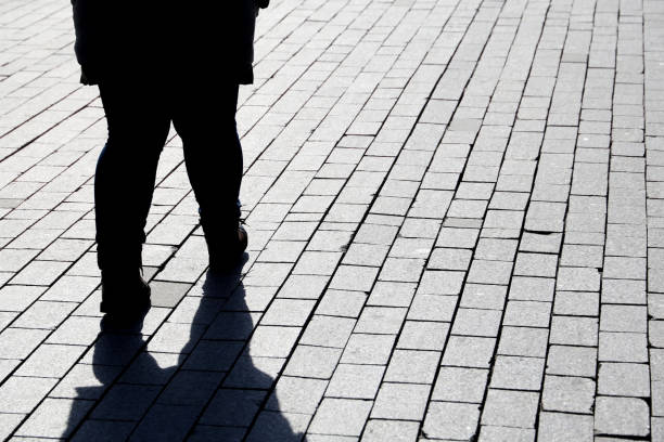istock Silhouette of fat woman walking down the street, black shadow on pavement 1385644973